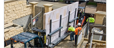 Workers are supervised loading large acrylic windows onto a trolley.